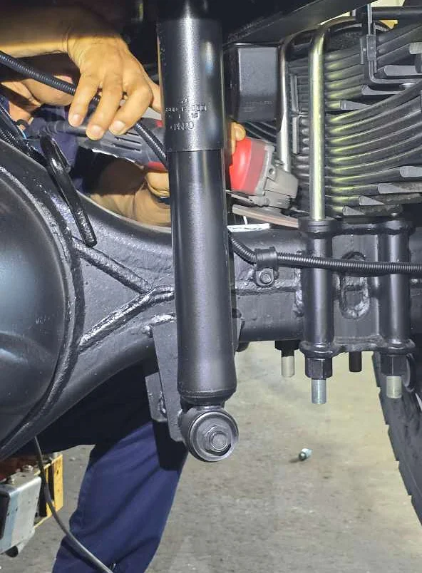 Technician fitting a GX-6 sensor from under the truck — hands on the axle